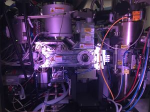 A photo gives a look inside a cryogenic electronic microscope. A collection of steel parts, tubes and wires of various colors are illuminated by a soft purple light.