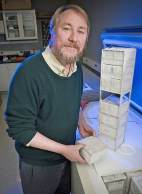Richard Lenski in his lab standing next to a freezer containing E. coli samples. 